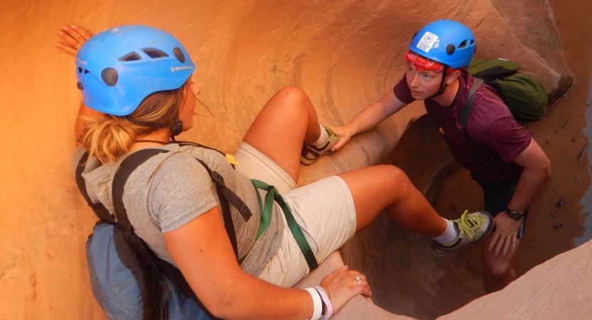 One person helps another maneuver a drop in a slot canyon. 